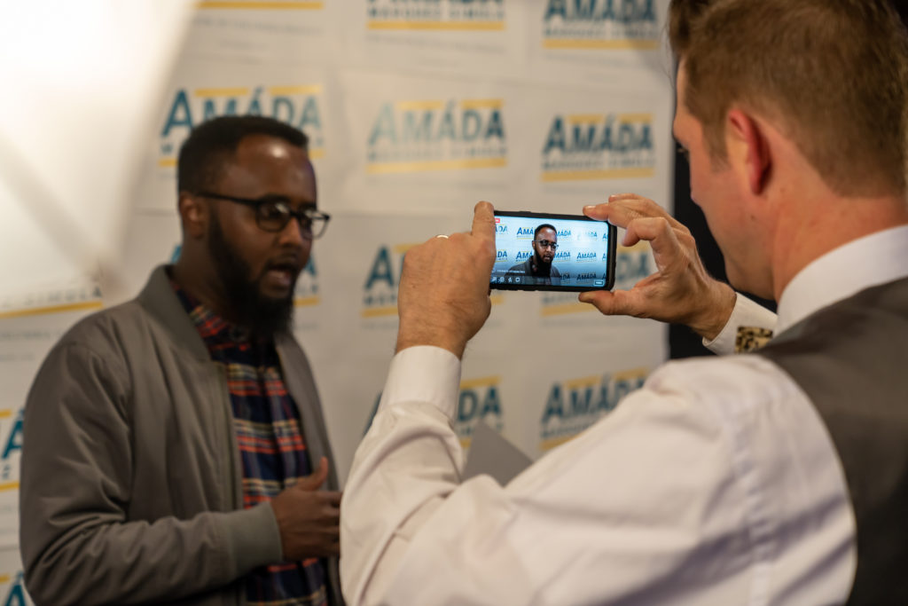 A Somali man is recorded on video in front of a backdrop for Amáda Márquez Simula.