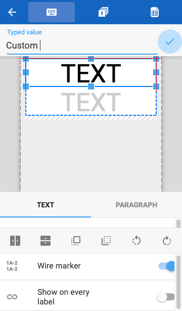 A label editor concept, showing a label with the word TEXT repeated twice. Icons for a keyboard, a sequence, and a spreadsheet are shown across the top of the screen. A text entry field is shown next, followed by a blue checkmark with pulsing blue halo. The bottom property sheet has tabs for Text and Paragraph that contain a number of positioning controls, such as align to center, bring to front, send to back, rotate left, rotate right, and so on.