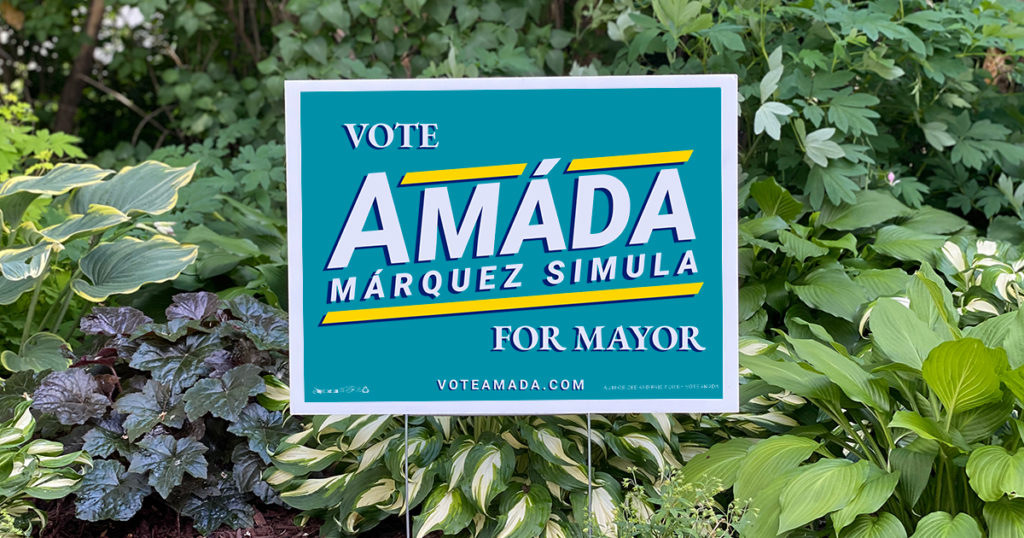A teal colored political campaign lawn sign reads Vote Amáda Márquez Simula for Mayor. voteamada.com