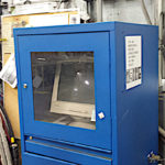 An old computer with a CRT monitor is locked inside a blue metal cabinet with a glass door.